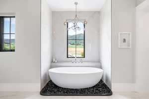 Bathroom with a freestanding tub, a chandelier, light marble finish flooring, and a mountain view