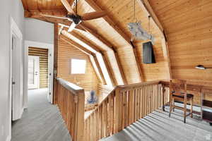 Hall with an upstairs landing, wooden ceiling, carpet, and rustic walls