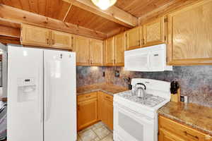 Kitchen with white appliances, a wood ceiling with exposed beams, decorative backsplash, and light stone finish floors