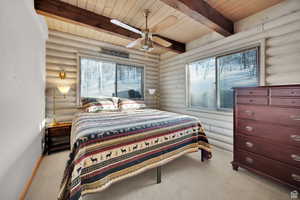 Carpeted bedroom featuring log walls, a wood ceiling with exposed beams, ceiling fan, and multiple windows