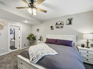 Bedroom with dark colored carpet, ceiling fan, and ensuite bathroom