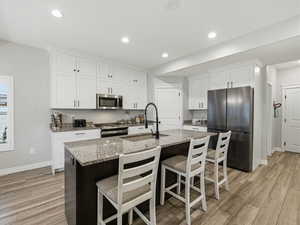 Kitchen featuring stainless steel appliances, white cabinets, a kitchen bar, light stone counters, and recessed lighting