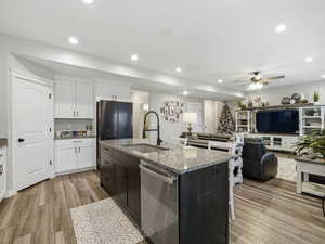 Kitchen with white cabinetry, stainless steel dishwasher, light stone counters, a breakfast bar, and an island with sink