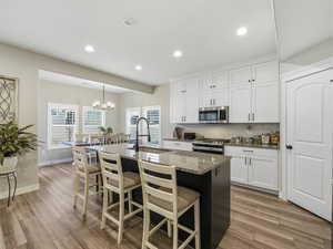 Kitchen featuring white cabinets, dark stone counters, a breakfast bar area, an island with sink, and recessed lighting