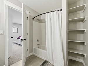 Ensuite bathroom featuring a textured ceiling, shower / bath combination with curtain, light tile patterned flooring, and light carpet