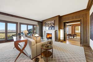 Living room with a lit fireplace, wood walls, wood finished floors, and crown molding