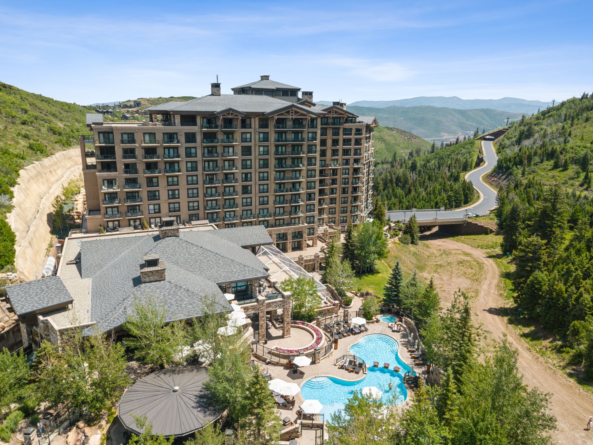 Multi-story building featuring numerous balconies, a complex roofline, and visible mountain scenery