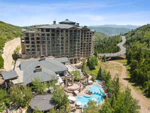 Multi-story building featuring numerous balconies, a complex roofline, and visible mountain scenery