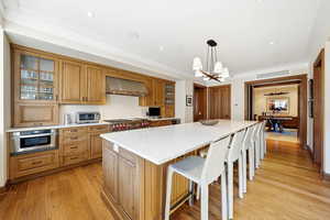 Kitchen with glass insert cabinets, decorative light fixtures, a breakfast bar, light wood-style floors, and brown cabinets
