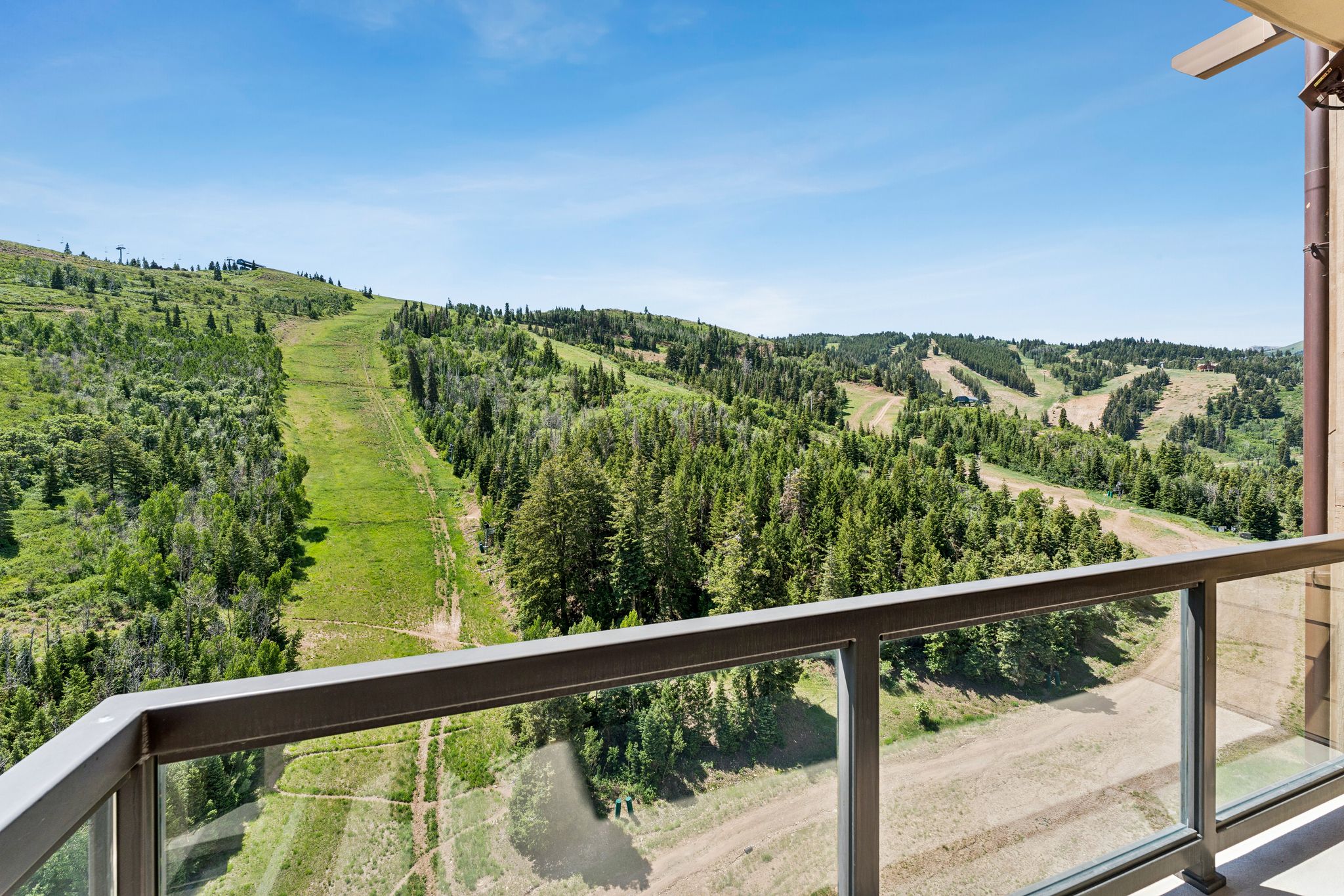 Balcony with glass railing overlooking mountainous terrain with forested areas and ski runs