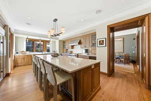 Kitchen with a center island, brown cabinetry, light wood-style floors, glass insert cabinets, and pendant lighting
