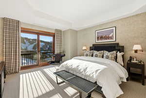 Carpeted bedroom featuring wallpapered walls, a water view, access to exterior, and a tray ceiling