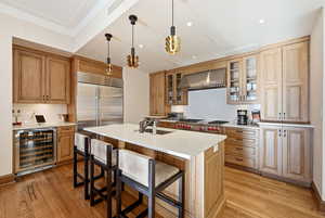 Kitchen featuring decorative light fixtures, a kitchen breakfast bar, glass insert cabinets, wine cooler, and wall chimney range hood