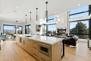 Kitchen with open floor plan, hanging light fixtures, light wood finished floors, recessed lighting, and light brown cabinetry