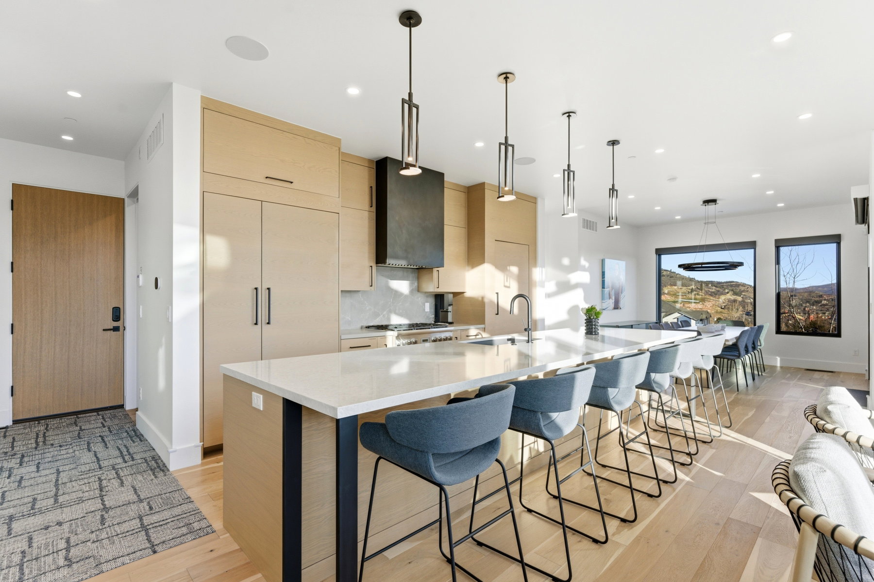 Kitchen with modern cabinets, light brown cabinetry, light stone countertops, pendant lighting, and a spacious island