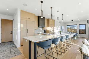 Kitchen with modern cabinets, light brown cabinetry, light stone countertops, pendant lighting, and a spacious island