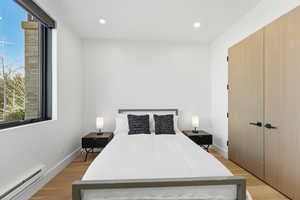 Bedroom with a baseboard radiator, a closet, light wood-style floors, and recessed lighting