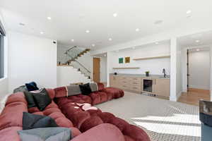 Living area featuring bar with sink, stairs, beverage cooler, and recessed lighting