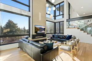 Living room featuring stairs, a towering ceiling, light wood-type flooring, a glass covered fireplace, and plenty of natural light