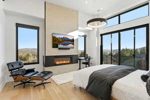 Bedroom with wood finished floors, a large fireplace, access to exterior, a high ceiling, and recessed lighting
