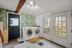 Washroom with wallpapered walls, beam ceiling, french doors, washer and clothes dryer, and tile patterned floors