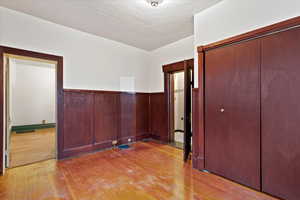 Unfurnished bedroom with wainscoting, a textured ceiling, light wood-style floors, and a closet