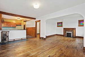 Unfurnished living room with dark wood-type flooring, arched walkways, wainscoting, a fireplace, and wooden walls