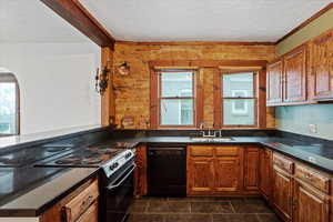 Kitchen with black appliances, brown cabinets, dark tile patterned flooring, a peninsula, and a textured ceiling