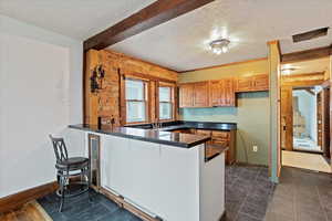 Kitchen featuring a kitchen bar, dark countertops, a peninsula, brown cabinetry, and a textured ceiling