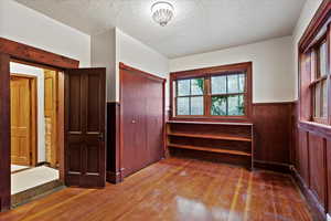 Unfurnished bedroom featuring a wainscoted wall, a closet, wood-type flooring, and a textured ceiling