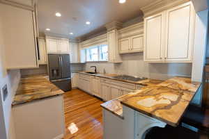 Kitchen with fridge with ice dispenser, recessed lighting, light wood finished floors, light stone countertops, and black electric stovetop
