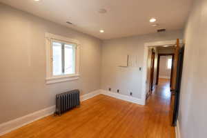 Empty room with radiator heating unit, light wood finished floors, and recessed lighting
