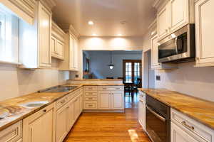Kitchen with black oven, stainless steel microwave, hanging light fixtures, light wood-type flooring, and a peninsula