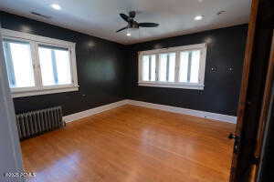 Empty room with radiator, wood finished floors, a ceiling fan, and recessed lighting. Also A/C and forced heat upstairs.