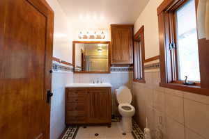 Full bathroom with light tile patterned floors, vanity, a shower, wainscoting, and tile walls