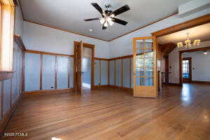 Unfurnished room with ceiling fan, crown molding, a chandelier, wood finished floors, and a decorative wall
