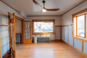Unfurnished dining area featuring radiator, light wood-type flooring, a ceiling fan, and crown molding
