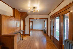 Corridor with a chandelier, ornamental molding, radiator heating unit, and light wood finished floors