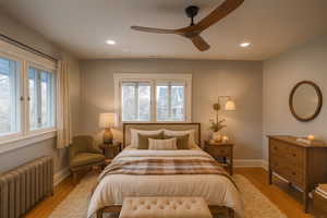 Bedroom with radiator heating unit, wood finished floors, ceiling fan, and recessed lighting