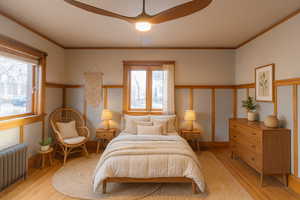 Bedroom featuring radiator heating unit, wood finished floors, crown molding, ceiling fan, and multiple windows