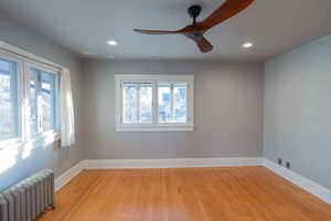 Unfurnished room with radiator, healthy amount of natural light, light wood-type flooring, a ceiling fan, and recessed lighting