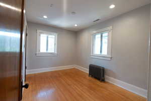 Spare room with radiator heating unit, light wood finished floors, healthy amount of natural light, and recessed lighting