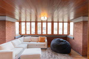Living area featuring brick wall, plenty of natural light, wooden ceiling, and wood finished floors
