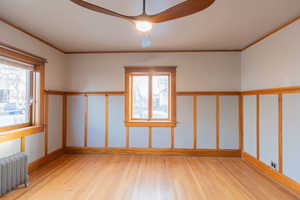 Empty room with radiator heating unit, light wood finished floors, crown molding, and plenty of natural light