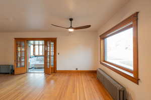 Empty room with radiator heating unit, light wood-type flooring, french doors, and ceiling fan