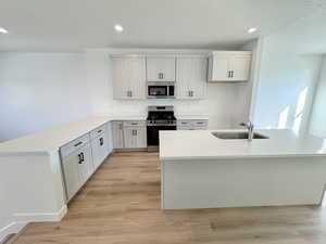 Kitchen with stainless steel appliances, light stone counters, recessed lighting, a peninsula, and light wood-type flooring