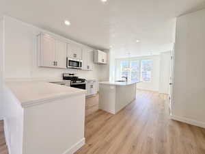 Kitchen featuring stainless steel appliances, a kitchen island with sink, light wood-style floors, recessed lighting, and light stone countertops