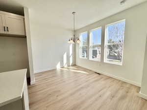 Unfurnished dining area featuring light wood-type flooring, a textured ceiling, and a chandelier