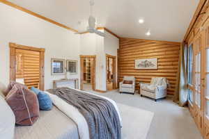 Carpeted bedroom with rustic walls, a ceiling fan, a spacious closet, high vaulted ceiling, and ornamental molding