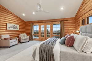 Carpeted bedroom with access to exterior, rustic walls, ceiling fan, and high vaulted ceiling